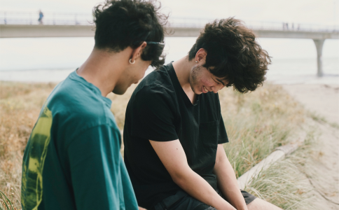 Two male friends laughing at beach sitting