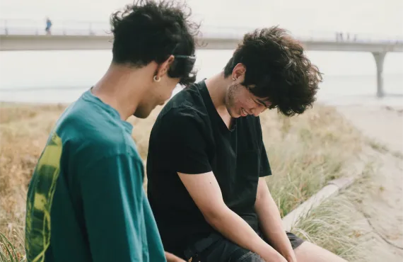 Two male friends laughing at beach sitting